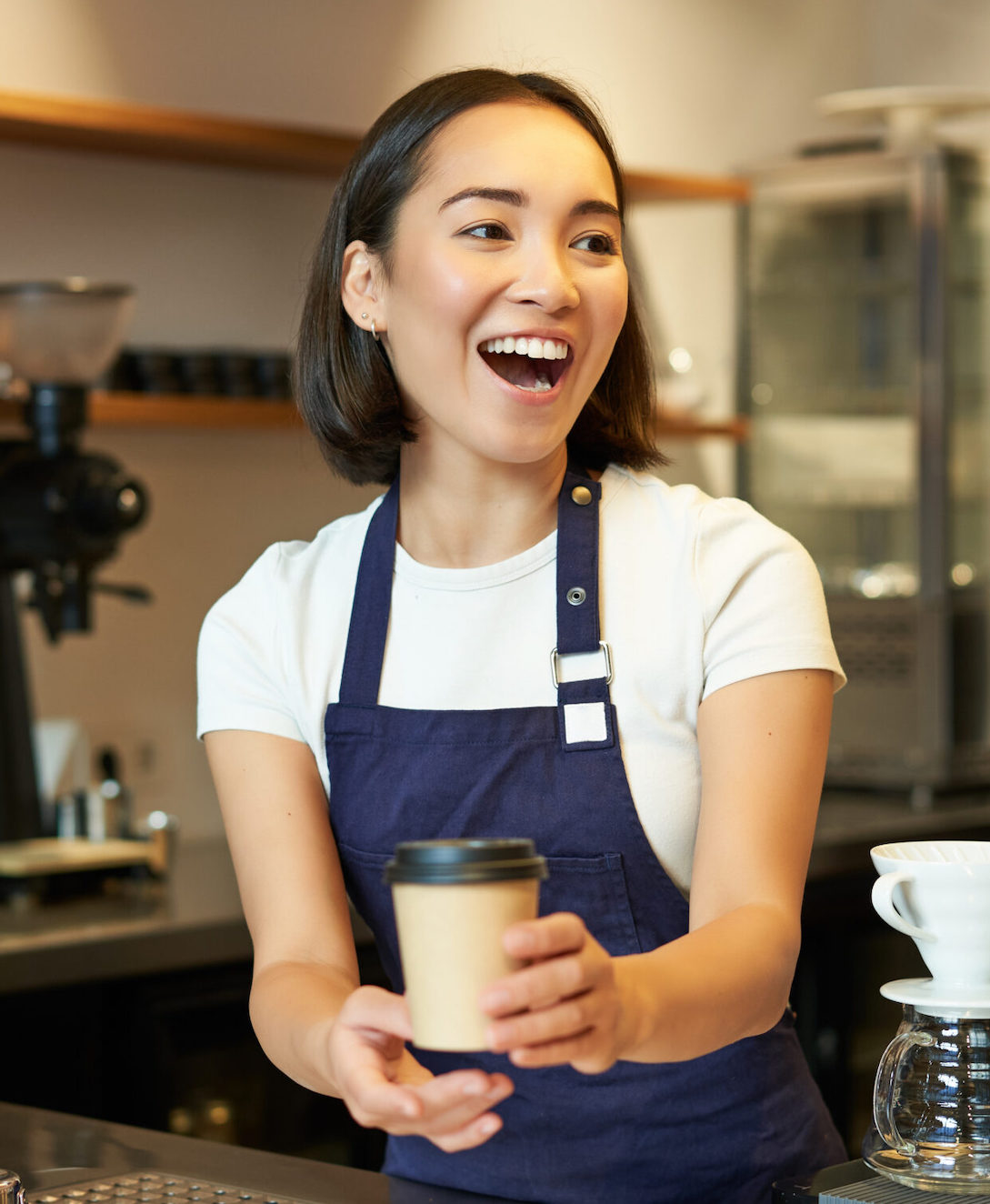 A brunette laughs, holding a coffee cup.